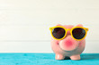 Happy piggy bank with sunglasses on color table against white wooden background, space for text. Finance, saving money