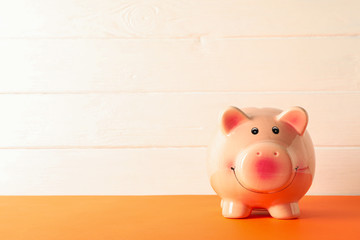  Happy piggy bank on color table against white wooden background, space for text. Finance, saving money