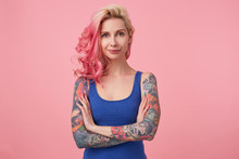 Portrait Of Positive Cute Lady With Pink Hair And Tattooed Hands, Standing Over Pink Background And Smiling, Wearing A Blue Shirt. People And Emotion Concept.