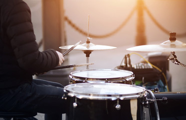 A street musician, wearing a jacket and jeans, plays with battered drumsticks on a drum set.