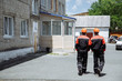 © bazil76 - Two men walking in the working clothes, wearing orange helmets. Two workers in special clothes walking along the street.