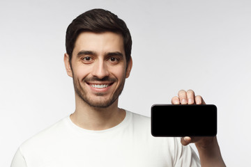 Young smiling man showing blank screen smartphone in hand, isolated on gray background