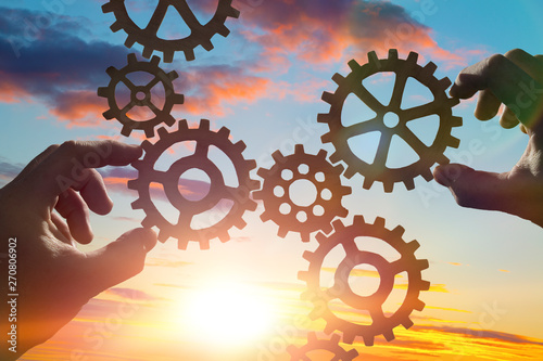 Fotografía Hands collect gear in a puzzle against the sky in the sunset