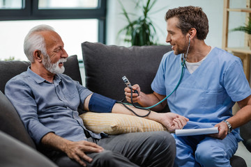 Wall Mural - Happy general practitioner measuring blood pressure of mature man while being in a home visit.