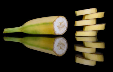 Half sweet yellow banana and a pyramid of slices with bright reflection in the glass on a contrasting black background