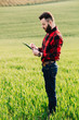 © anatoliycherkas - Young handsome bearded farmer with folder standing in green wheat field in early summer