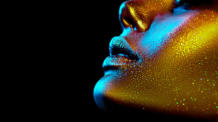 Wall Mural - Fashion model woman skin face in bright sparkles, colorful neon lights, beautiful sexy girl lips, mouth. Trendy glowing gold skin make-up. Art design make up. Glitter metallic shine makeup