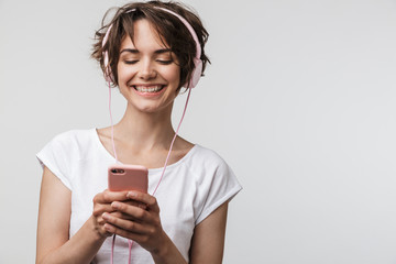 Wall Mural - Image of smiling woman in basic t-shirt holding smartphone while listening to music with headphones