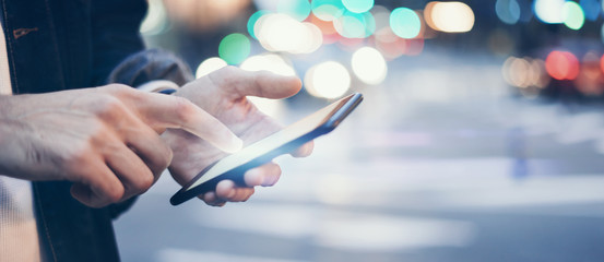 Closeup image of male hands with smartphone at night on city street, searching internet or social networks, hipster man typing an sms message on chat