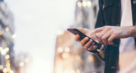 Closeup image of male hands with smartphone at night on city street, searching internet or social networks, hipster man typing an sms message on chat