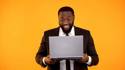 Wall Mural - Joyful black businessman receiving news on laptop, Successful startup, winner