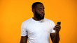 © motortion - Afro-American man holding smartphone isolated on yellow background, technology