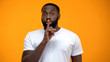 © motortion - African-American man showing silence gesture, keeping secret, yellow background