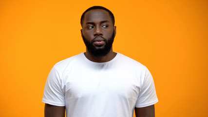 Ashamed African-American man looking to side against yellow background, guilty