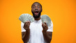 © motortion - Astonished Afro-American man holding bunches of dollars, lucky lottery winner