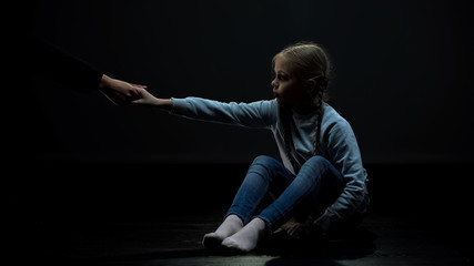 Wall Mural - Little child in dark room accepting adult helping hand, social security concept