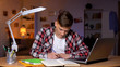 © motortion - Teenager doing his homework, writing task into copybook, laptop on table
