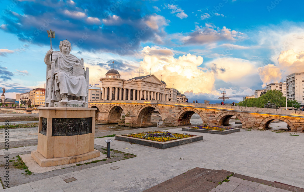 Obraz na płótnie SKOPJE, NORTH MACEDONIA - 25.04.2019: Byzantine Emperor Justinian Statue and Stone Bridge, behind the Archeology Museum at sunset in Skopje w salonie