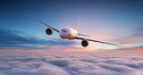 Fototapeta  - Commercial airplane jetliner flying above dramatic clouds in beautiful sunset light. Travel concept.