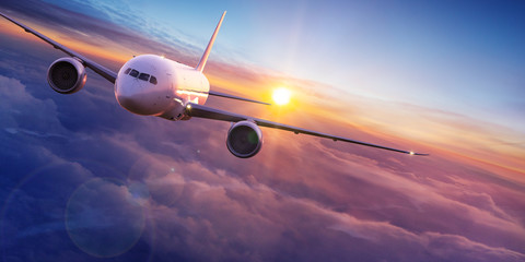 Commercial airplane jetliner flying above dramatic clouds in beautiful sunset light. Travel concept.