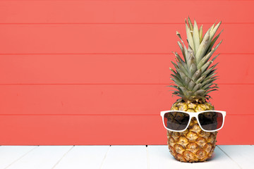 hipster pineapple with sunglasses against a living coral colored wood background. minimal summer con