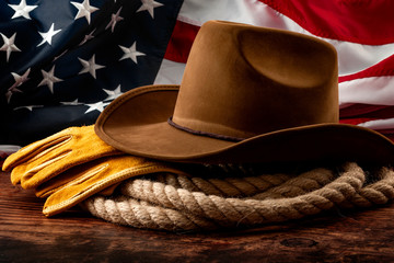 Fototapete - American culture, independence day in the United States of America and 4th of july concept theme with a cowboy hat, USA flag, rope lasso and farm gloves on a wooden background in a old saloon