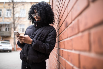 Wall Mural - Attractive young African woman holding a mobile phone reading a text message with a serious expression outdoors