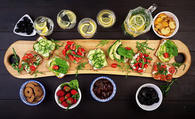 Flat lay of healthy vegetarian dinner table setting. Sandwiches with tomato, cucumber, avocado, strawberry, herbs and olives, snacks. Clean eating, vegan food