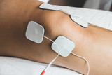 Fototapeta Zachód słońca - Patient applying electrical stimulation therapy on knee joint. Therapist placing electrodes on Knee. Electrical tens.