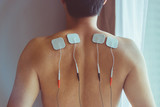 Fototapeta Zachód słońca - TENS treatment in physical therapy. Young man with TENS on his back and shoulders.