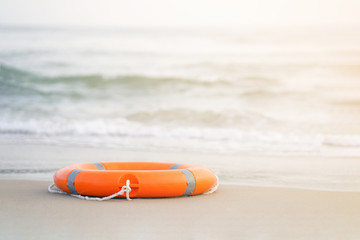 Wall Mural - Orange lifebuoy lies on the shore on a sunny day against the background of the sea. Red lifebuoy on the background of the ocean.  Life ring on the sea sand. Toning.