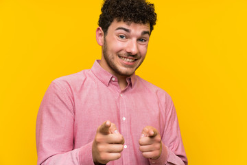 Man with curly hair over isolated yellow wall points finger at you