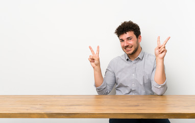 Young man with a table showing victory sign with both hands