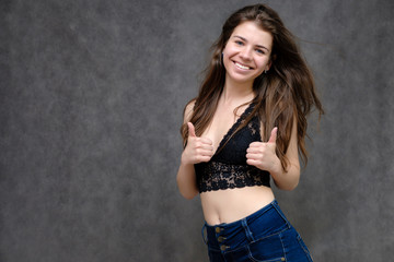 Photo portrait of a beautiful smiling brunette woman girl on a gray background in jeans and a blouse with long beautiful flowing dark hair in the studio.