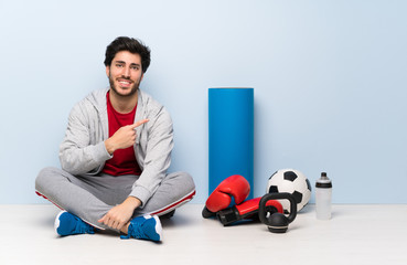 Sport man sitting on the floor pointing to the side to present a product