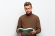 © luismolinero - Blonde man over isolated white wall holding a book and enjoying reading