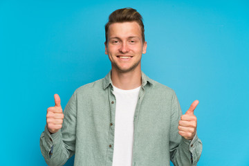 Blonde handsome man with green shirt giving a thumbs up gesture