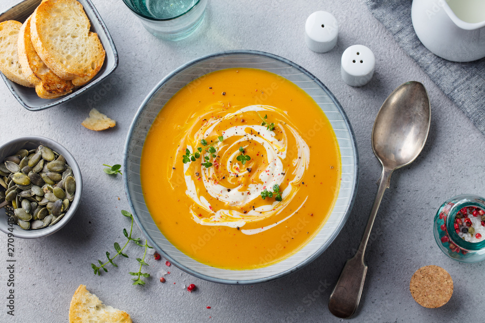 Pumpkin and carrot soup with cream on grey stone background. Top view. - obrazy, fototapety, plakaty 
