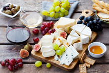 Cheese And Fruits Assortment On Cutting Board With Red, White Wine On Wooden Background.