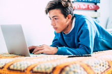 Teenager Alone At The Bedroom On The Bed Looking Videos, Working Or Play Videogames With His Laptop Or Computer And His Phone - Online Lifestyle And Future Generations