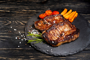 Wall Mural - juicy piece of fried meat lies on a stone plate against a black wooden table