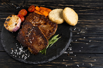 Wall Mural - juicy piece of fried meat lies on a stone plate against a black wooden table