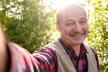 Selfie from handsome senior hispanic man on sunny day. Cheerful senior man making a photo on vacation