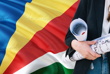 Seychellois Architect woman holding blueprint against Seychelles waving flag background. Construction and architecture concept.