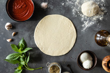 Top View Of Raw Dough, Ingredients And Spices For Pizza Margherita With Tomato Sauce And Mozzarella Cheese On Black Background.