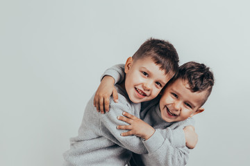 Photo of two adorable boys brothers or friends embracing and smiling joyfully on a gray background.