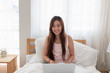 © weedezign - Asian woman wear top tank raise using laptop on bed in bedroom in morning,relax lifestyle concept.looking at camera