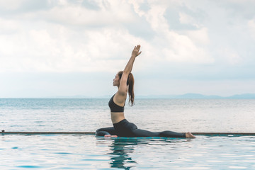 Wall Mural - Happy Asian woman wearing black sport wear practice yoga Pigeon pose on the pool above the beach with beautiful sea in Tropical island,Feeling comfortable and relax in holiday,Vacations Concept