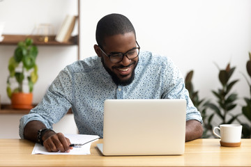 head shot smiling african-american manager using laptop looking at screen