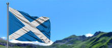 Scotland Flag Waving In The Blue Sky With Green Fields At Mountain Peak Background. Nature Theme.